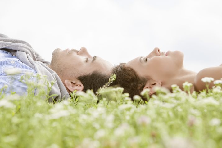 couple laying on the grass with the tops of their heads touching and their eyes closed