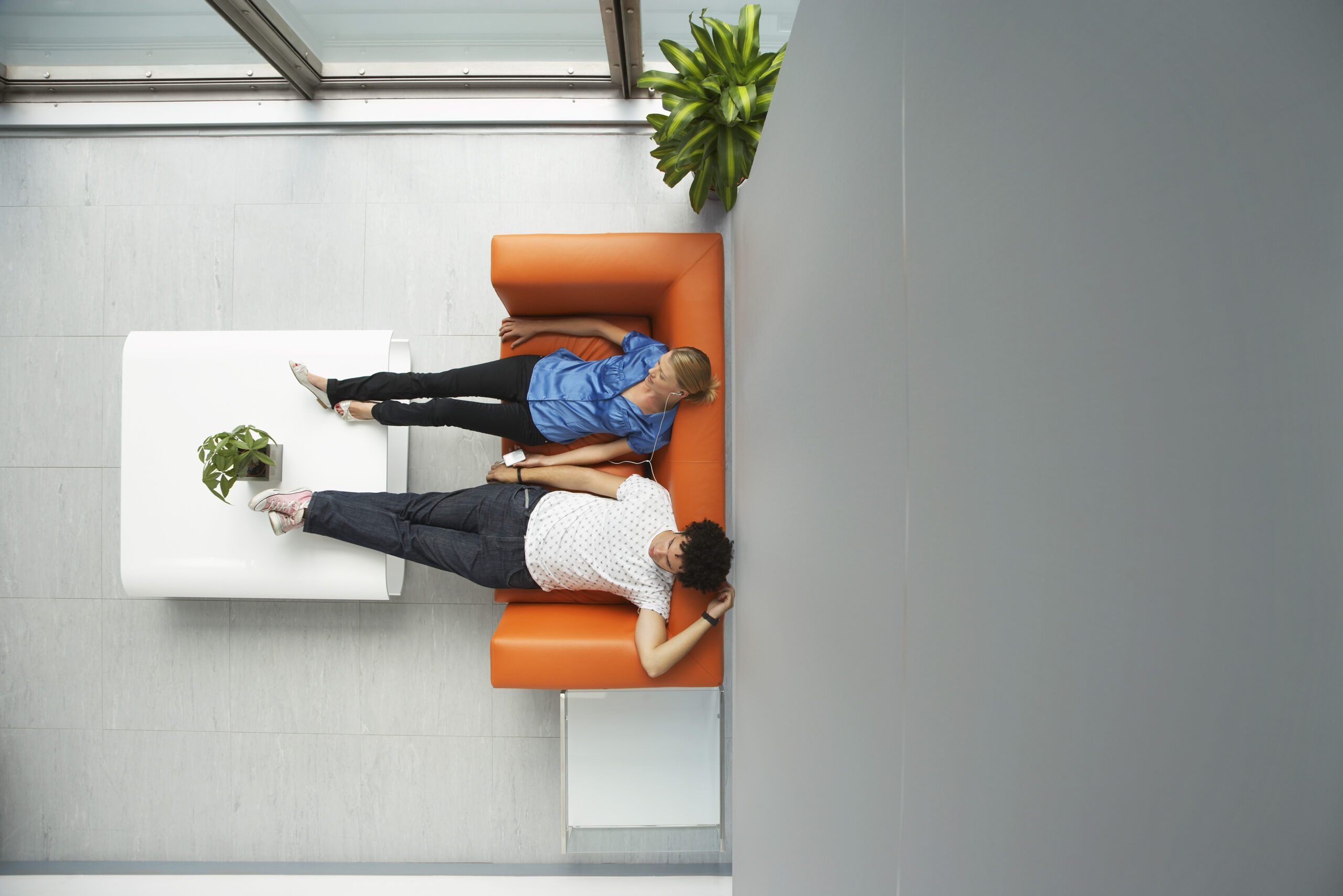 Aerial view of a man and a woman reclining on an orange couch with feet propped up on a coffee table.