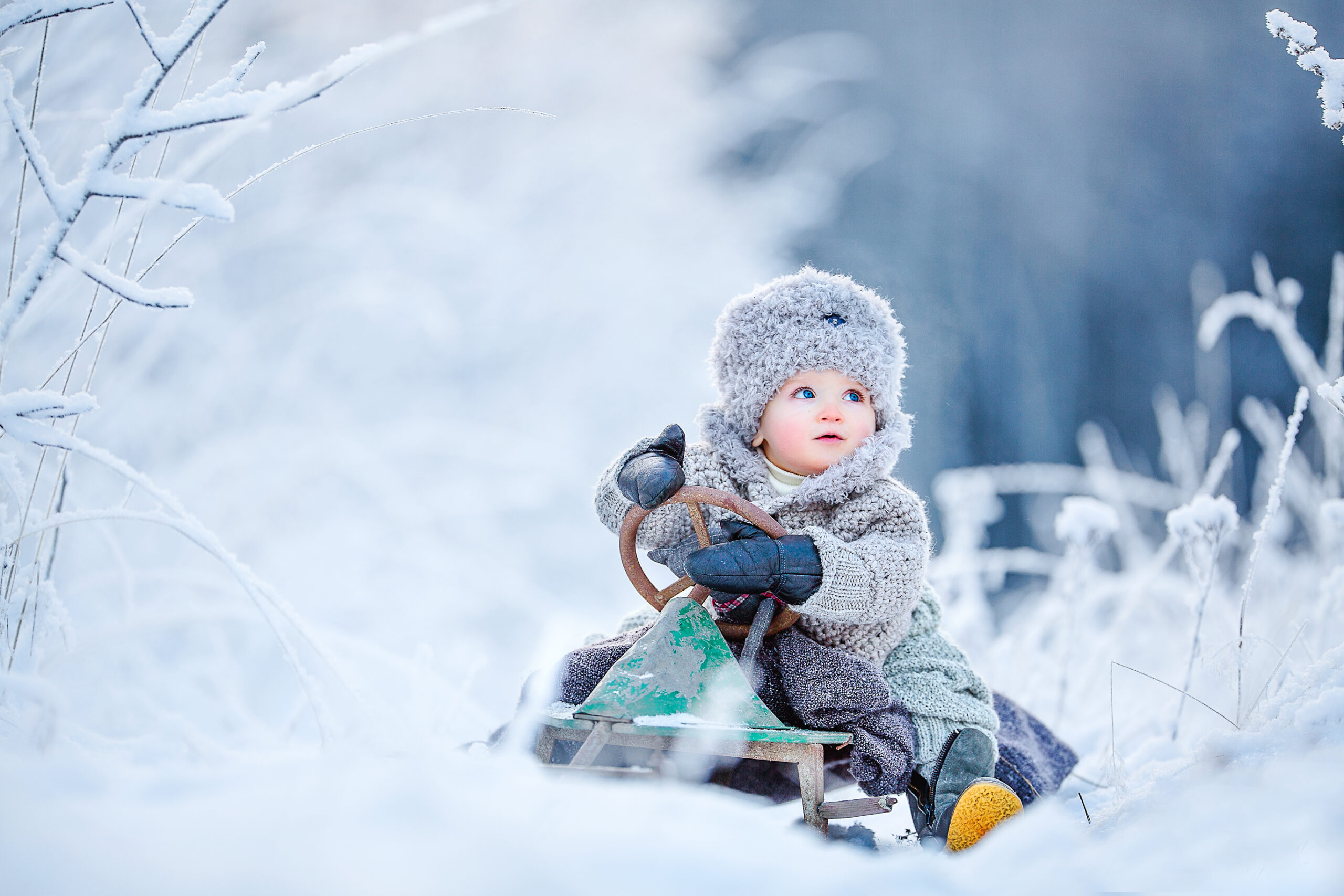 Child in green and white jacket sitting on snow-covered ground