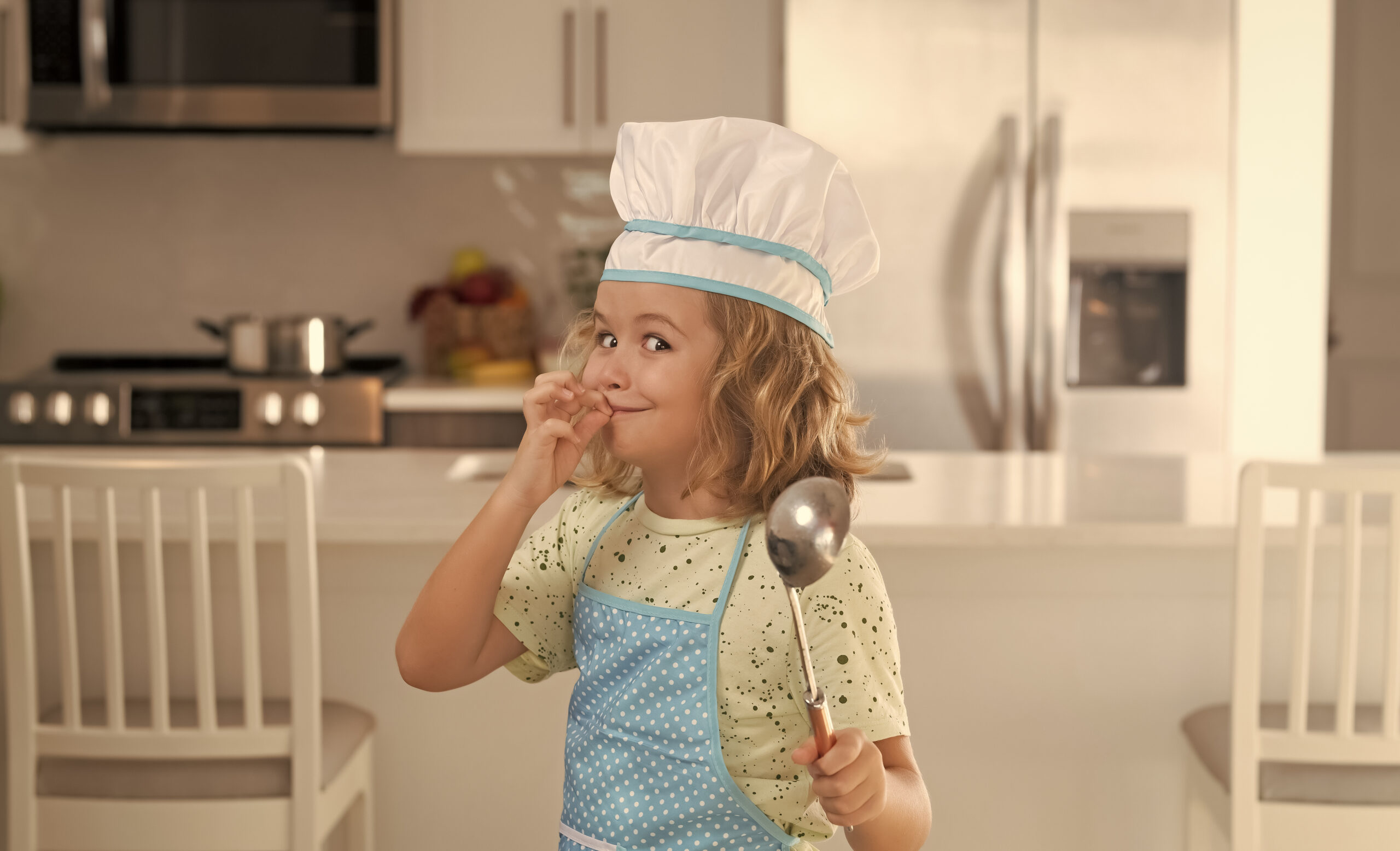 Kid chef cook wearing cooker uniform and chef hat preparing food on kitchen. 
