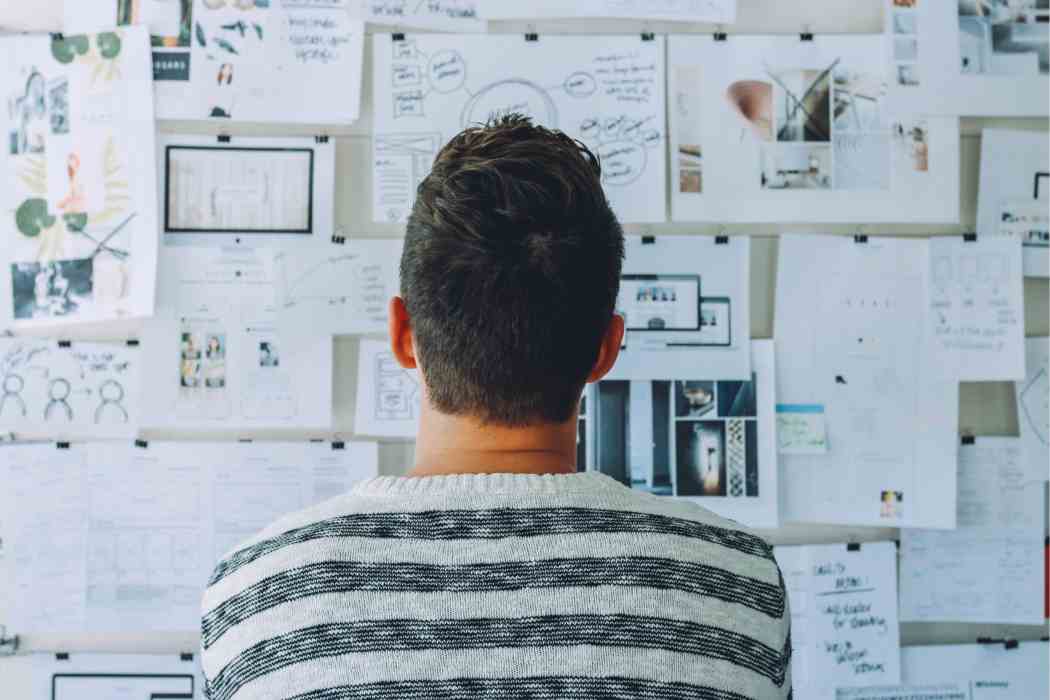 Man Wearing Black and White Stripe Shirt Looking at White Printer Papers on the Wall