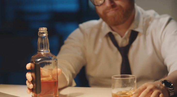 Stressed man sitting at a desk with a drink in hand, attempting to relieve work-related anxiety. Stressed man sitting at a desk with a drink in hand, attempting to relieve work-related anxiety.
