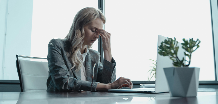 Woman sitting at her desk with a stressed expression, surrounded by work documents, highlighting the impact of professional stress on well-being. Woman sitting at her desk with a stressed expression, surrounded by work documents, highlighting the impact of professional stress on well-being.