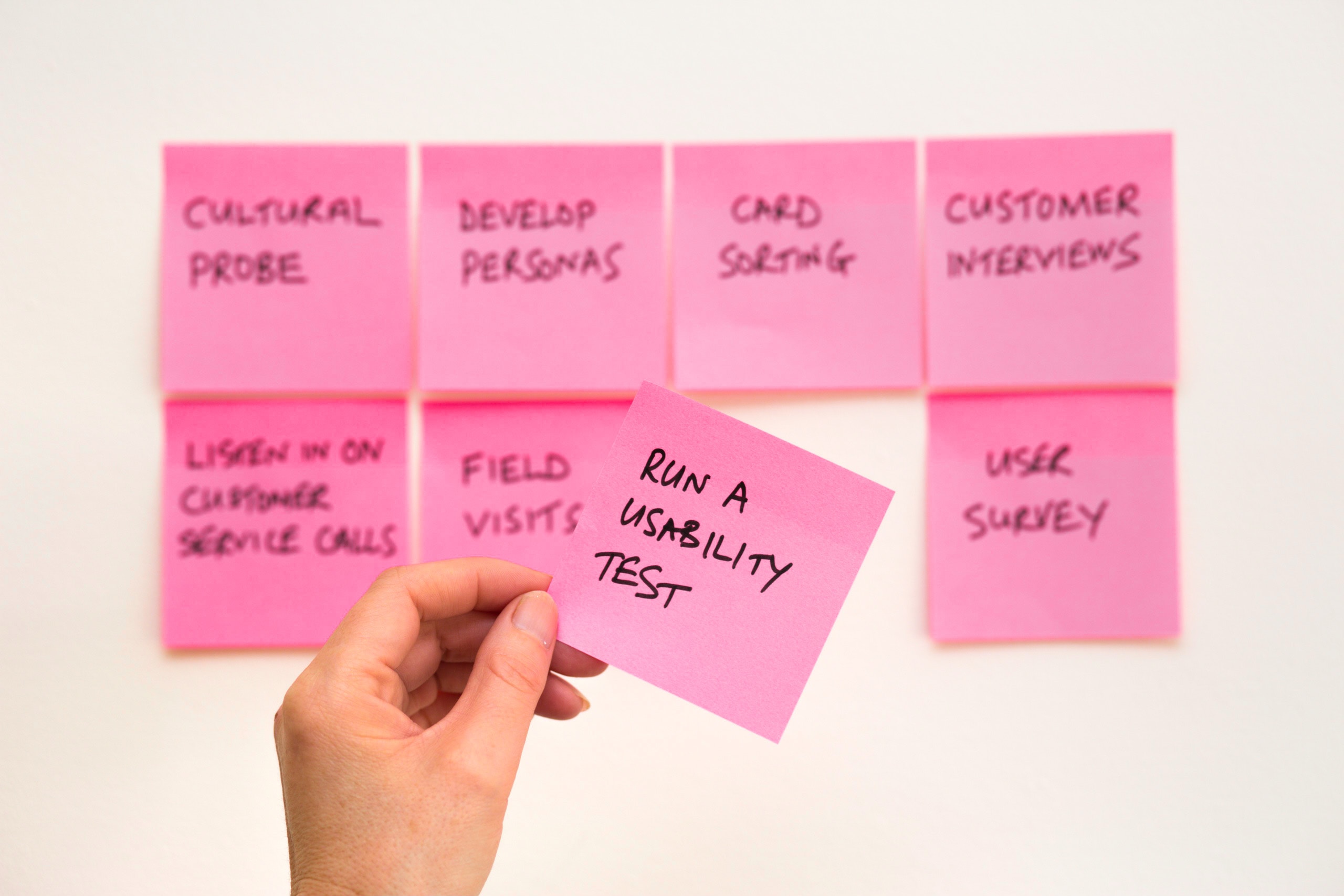 picture of pink post-it notes on a wall with a hand hold one up