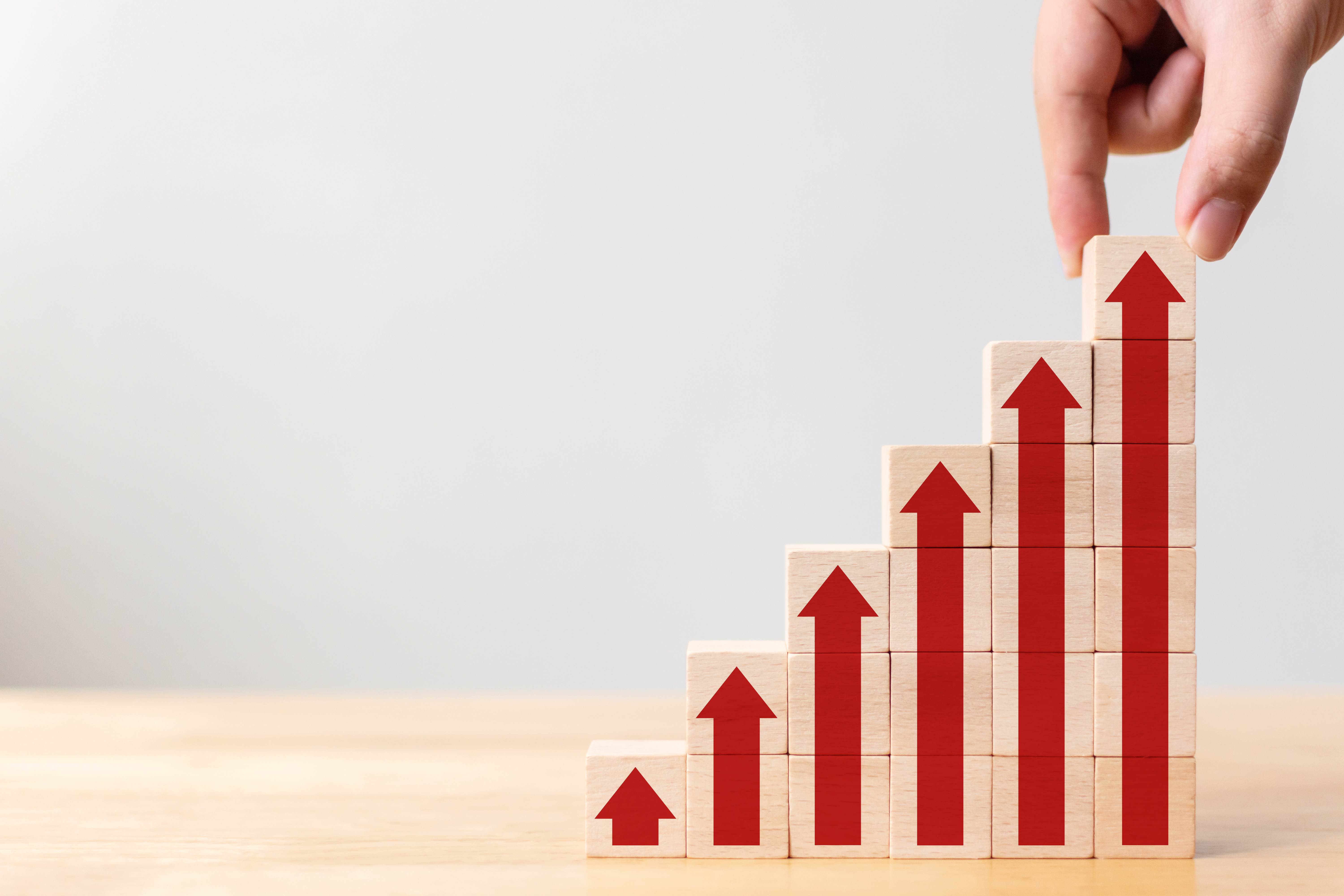 Stacked wooden blocks with red arrows pointing upward, symbolizing business growth, progress, and increased performance