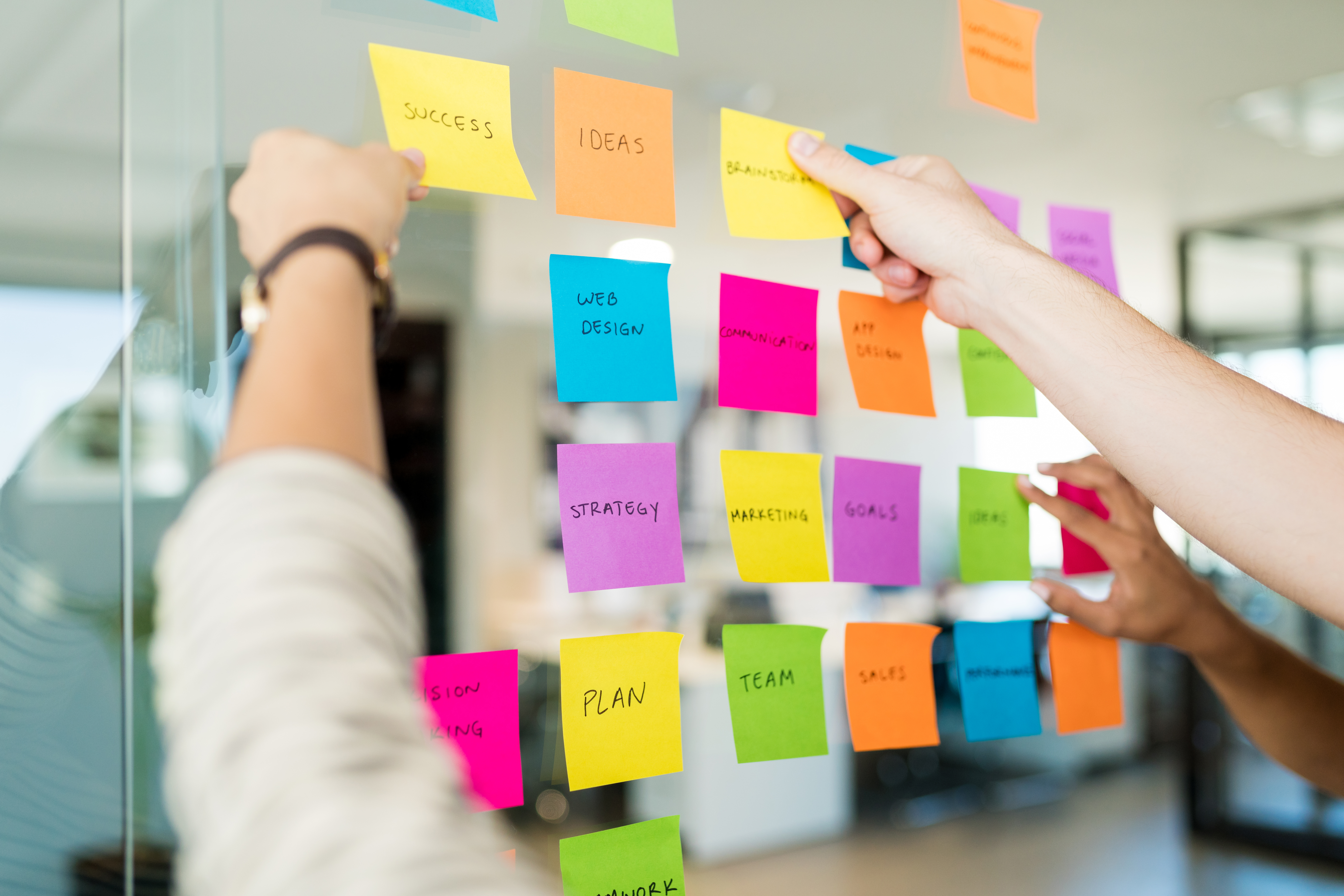 Colorful post-it notes on a glass wall, representing brainstorming ideas for business strategy, success, and teamwork.