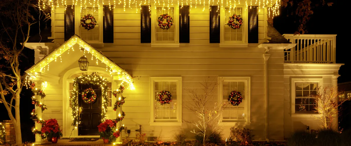 Traditional two-story house with warm yellow holiday lights and festive wreaths. Traditional two-story house with warm yellow holiday lights and festive wreaths.