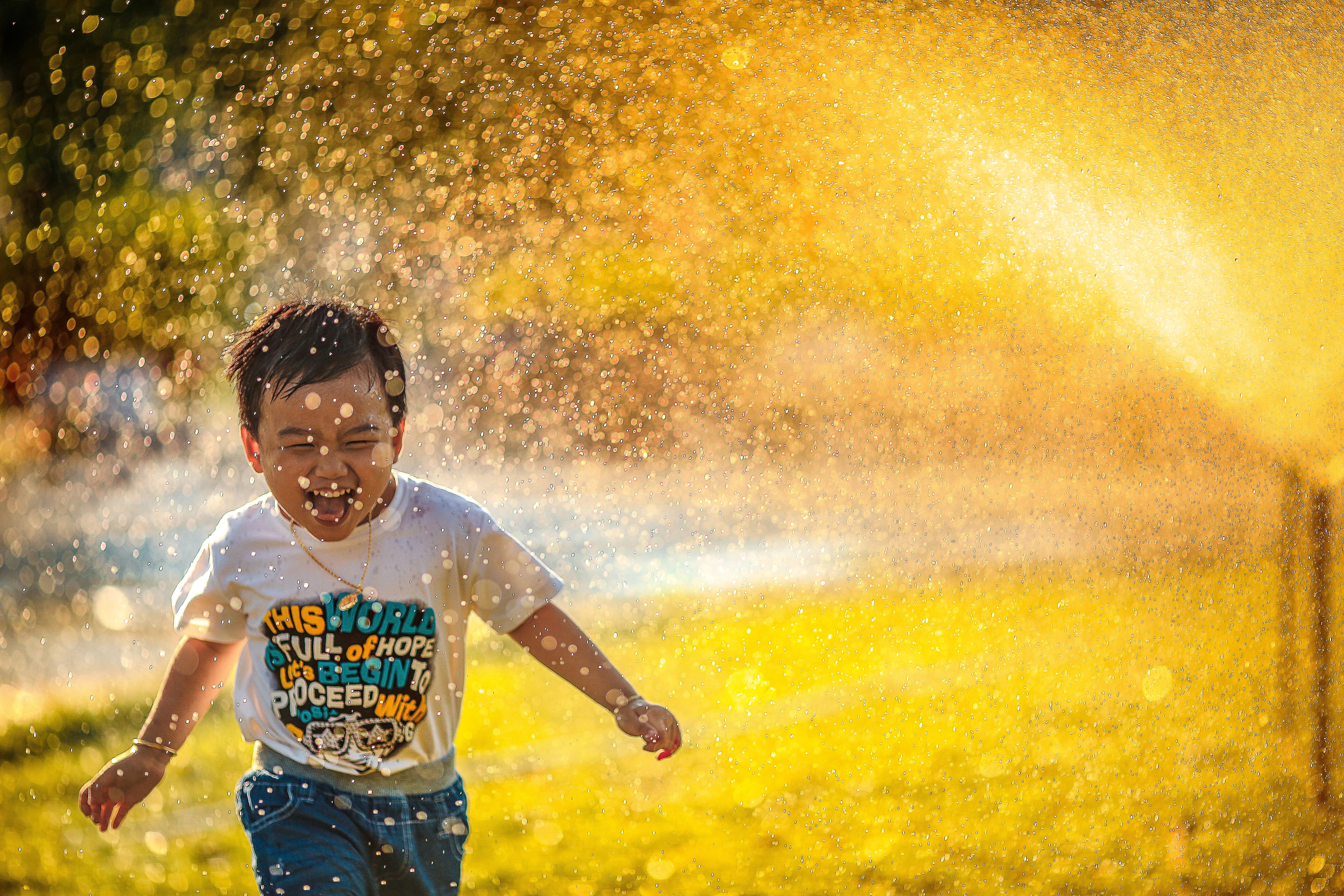 happy kid playing in the field with sprinklers