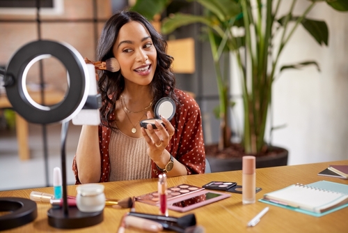 Beauty content creator applying makeup while filming tutorial with ring light and cosmetics on desk — influencer marketing in health and beauty industry Beauty content creator applying makeup while filming tutorial with ring light and cosmetics on desk — influencer marketing in health and beauty industry