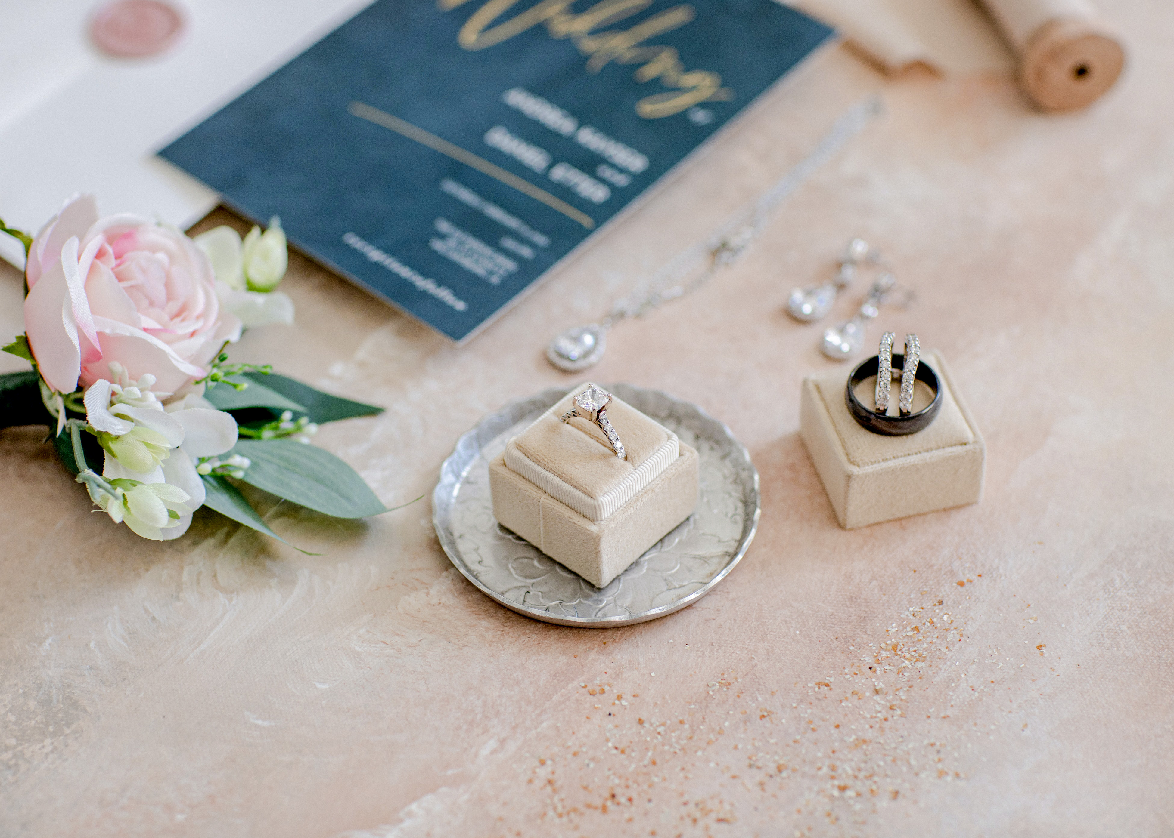 tan ring boxes with engagement ring and wedding bands and invitation suite in the background