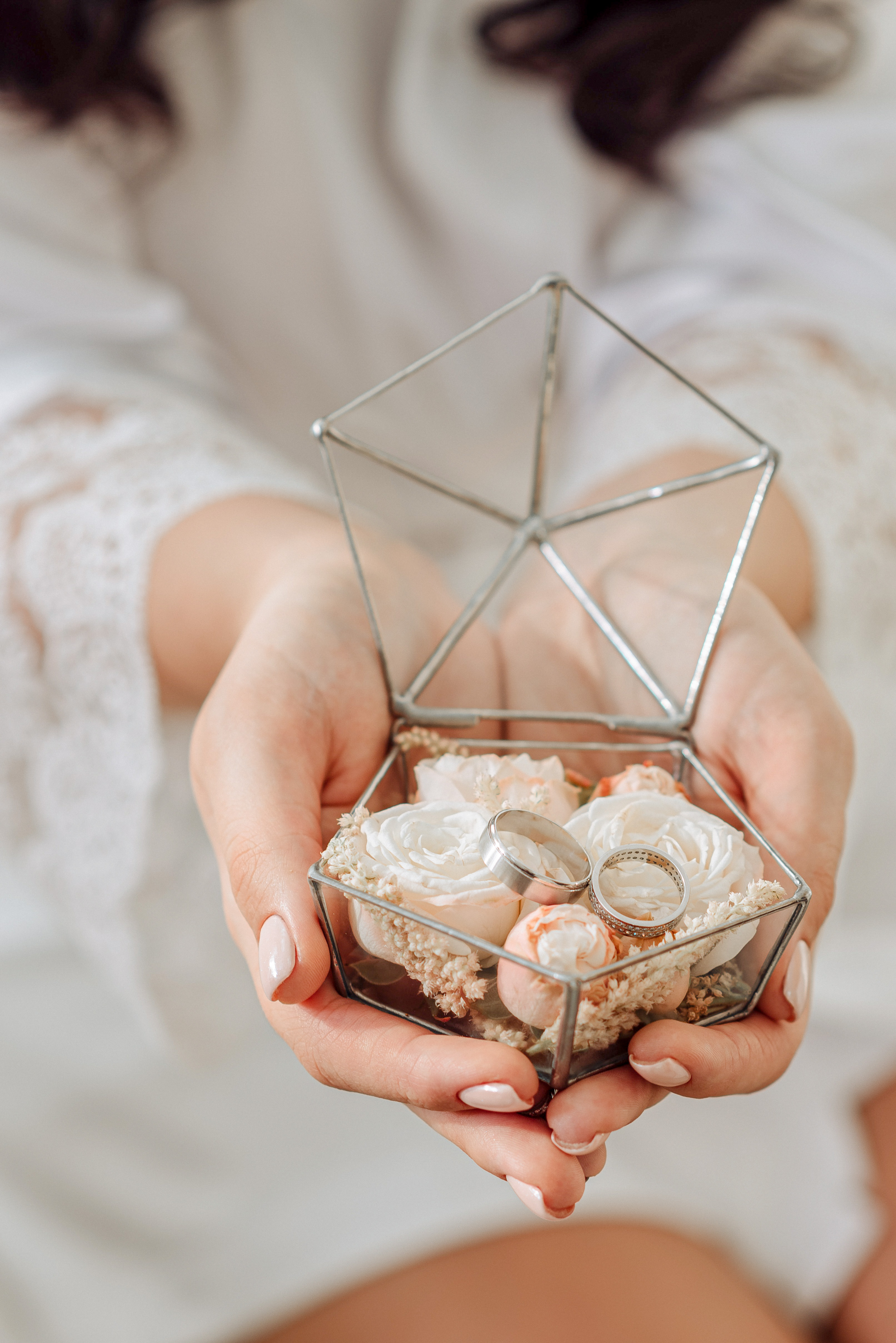 bride holds glass terrarium with seashells and silver wedding bands inside