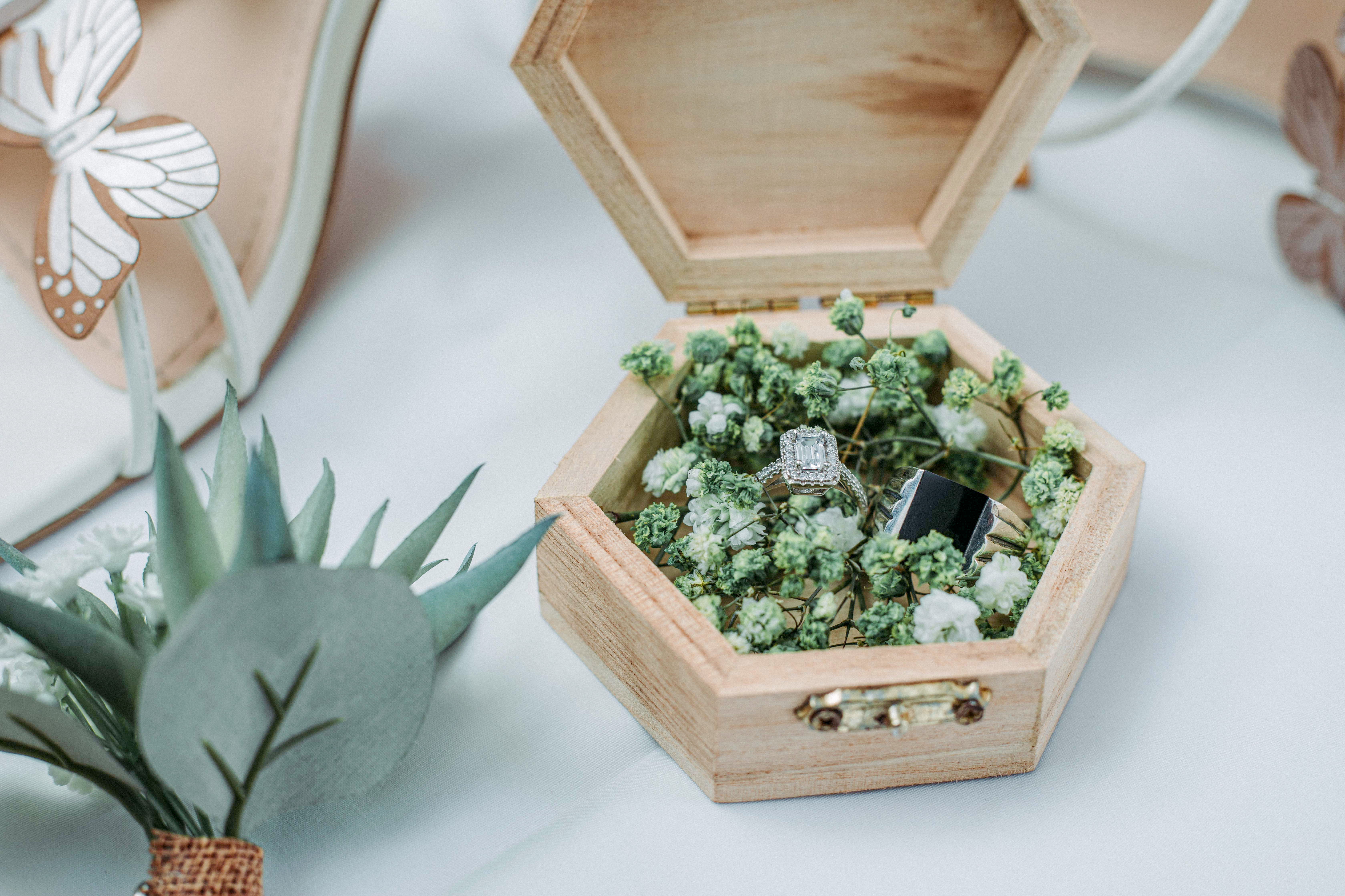 bride's shoes surround a wooden hexagon card box with an engagement ring and wedding band inside