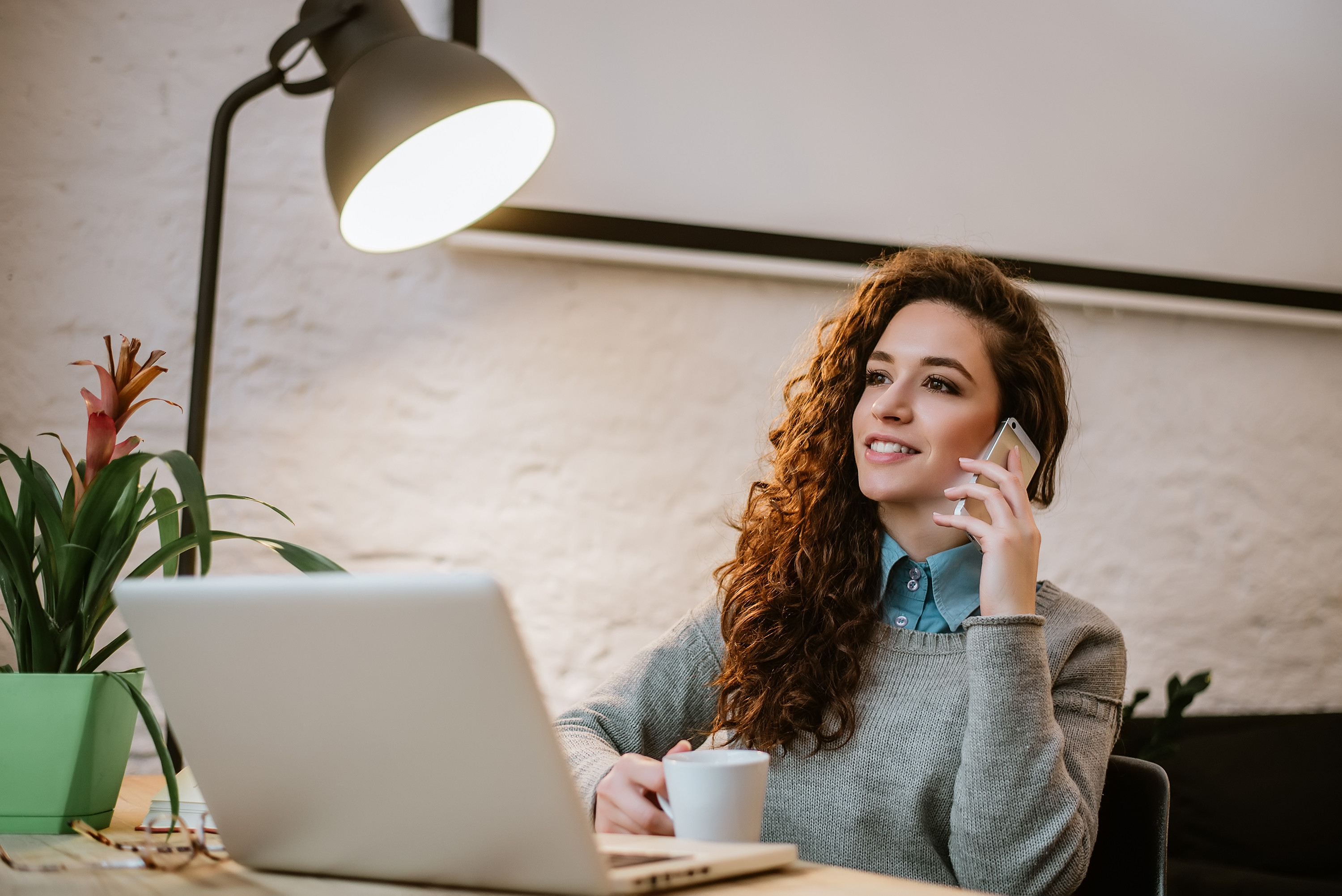 Businesswoman multitasking at her desk with a laptop and mobile phone discussing immediate callback solutions"