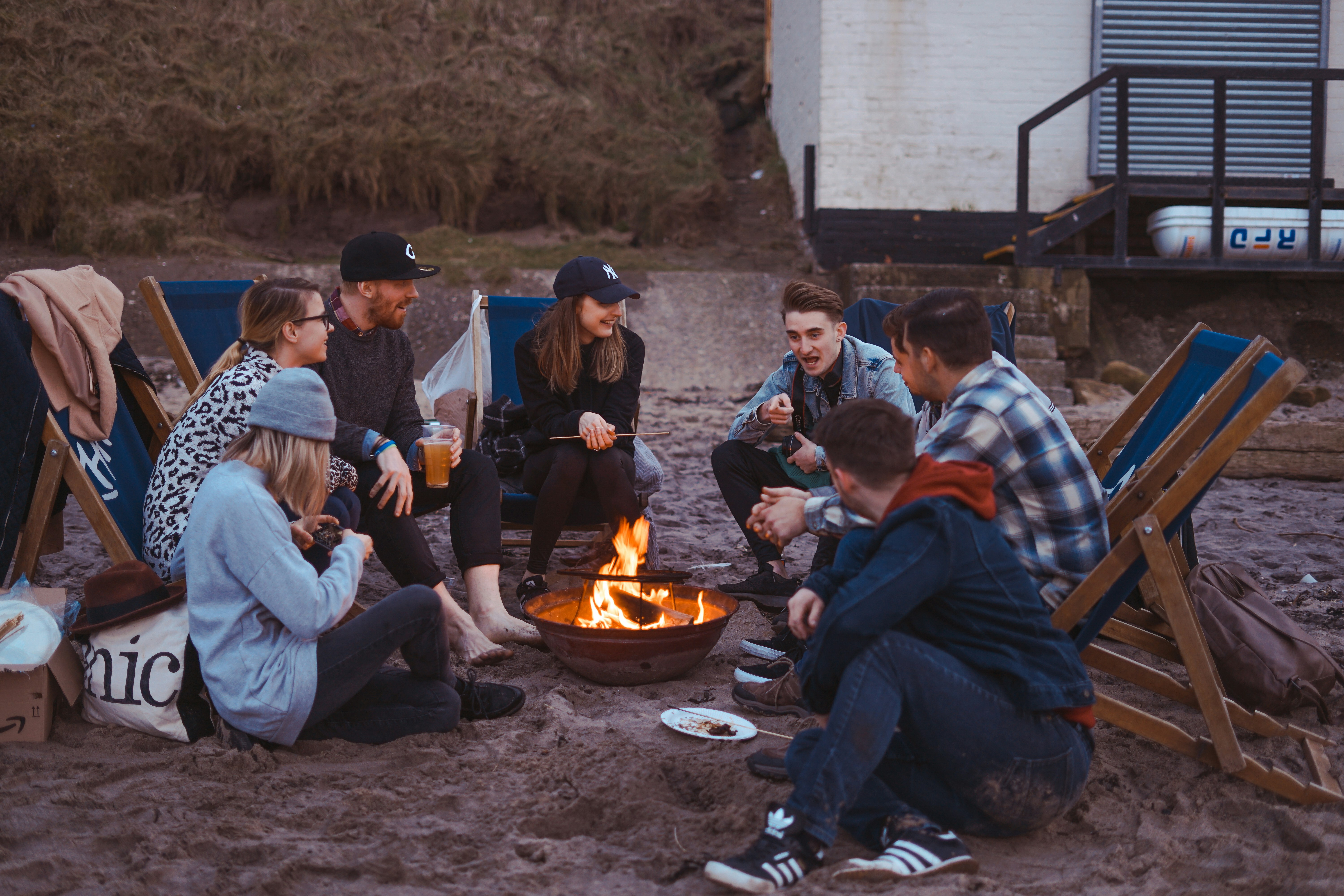 A beach scene with a group of individuals seated around a fire pit, creating a warm atmosphere as they relax together. A beach scene with a group of individuals seated around a fire pit, creating a warm atmosphere as they relax together.