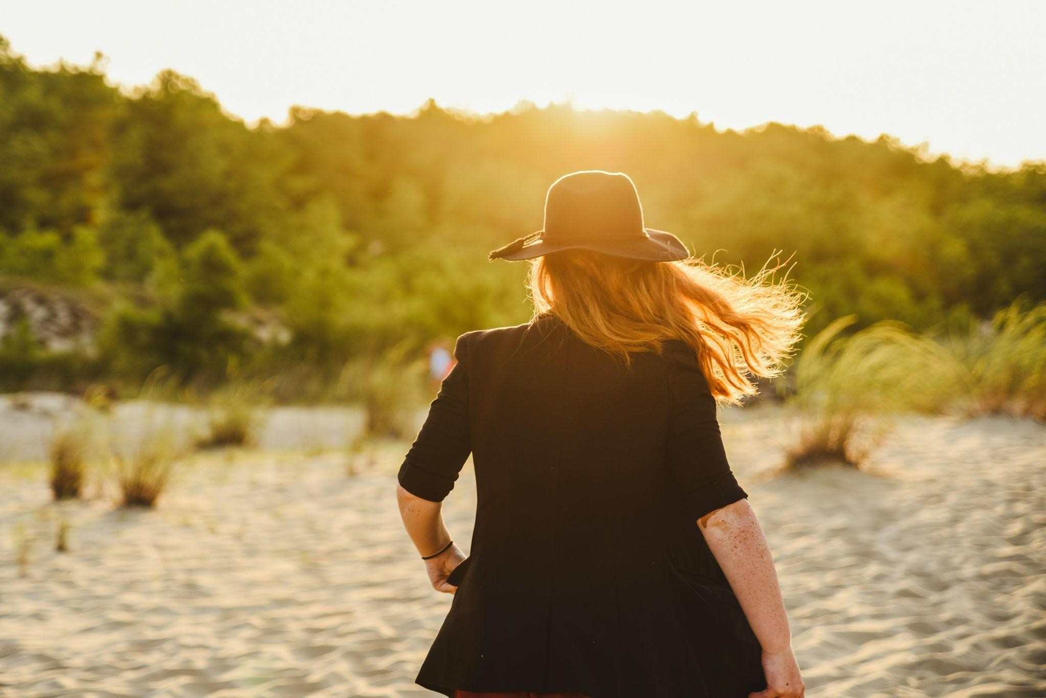 A woman in a hat and black jacket walks on the beach, with the ocean waves and sandy shore in the background. A woman in a hat and black jacket walks on the beach, with the ocean waves and sandy shore in the background.