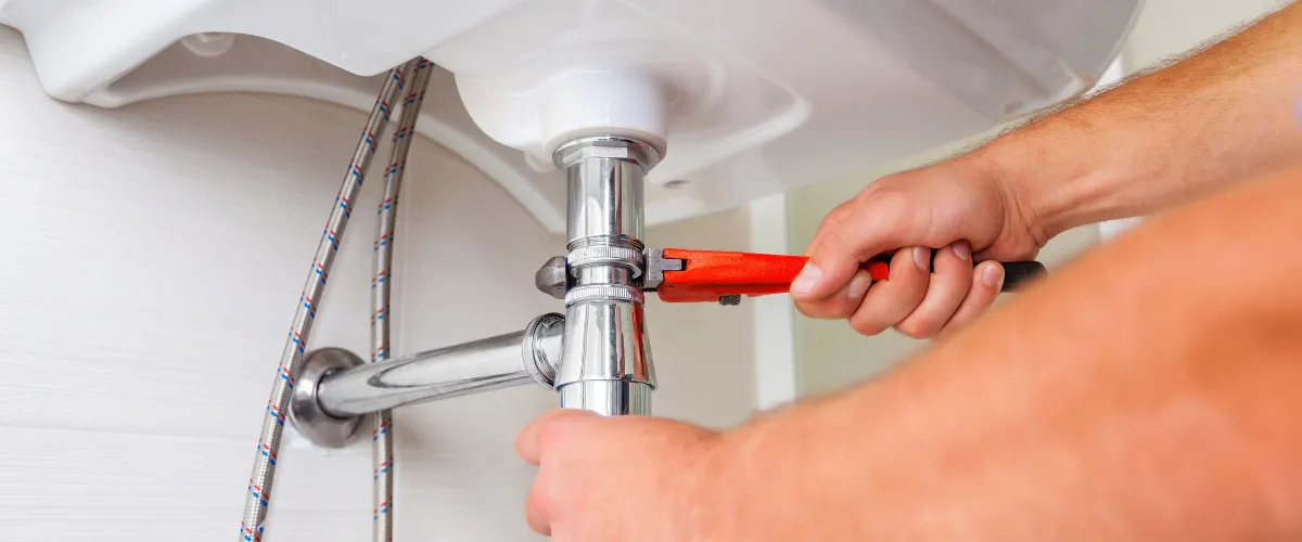 Plumber tightening sink pipe with wrench to fix leak Plumber tightening sink pipe with wrench to fix leak