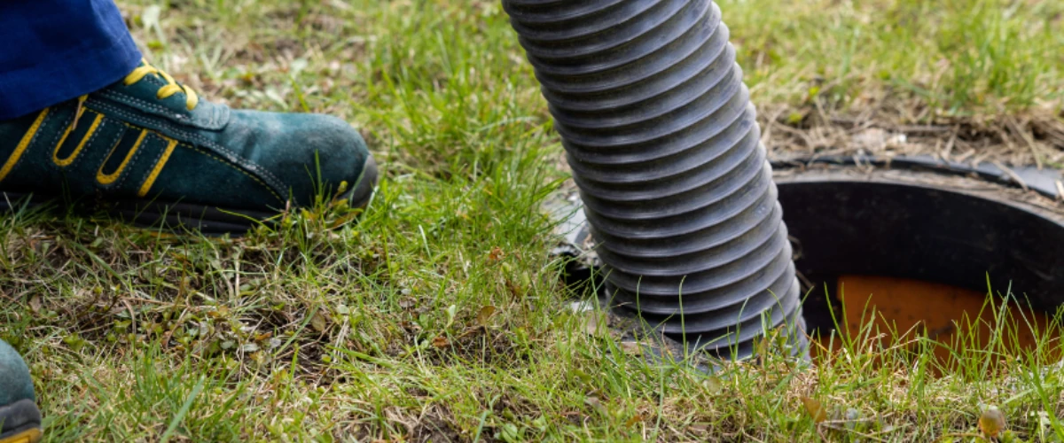 Technician performing septic tank pumping and cleaning using heavy-duty vacuum hose.