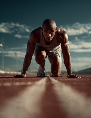 Male sprinter in starting position on track with intense determination, representing mental focus, process-driven concentration, and resilience under competitive pressure.