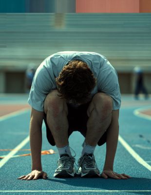 A young athlete crouches on a running track, head bowed in focus, preparing mentally to manage emotions before competition. A young athlete crouches on a running track, head bowed in focus, preparing mentally to manage emotions before competition.