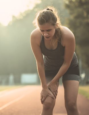 A female runner bends over in exhaustion on the track, highlighting signs of overreacting and the importance of listening to your body in sport.