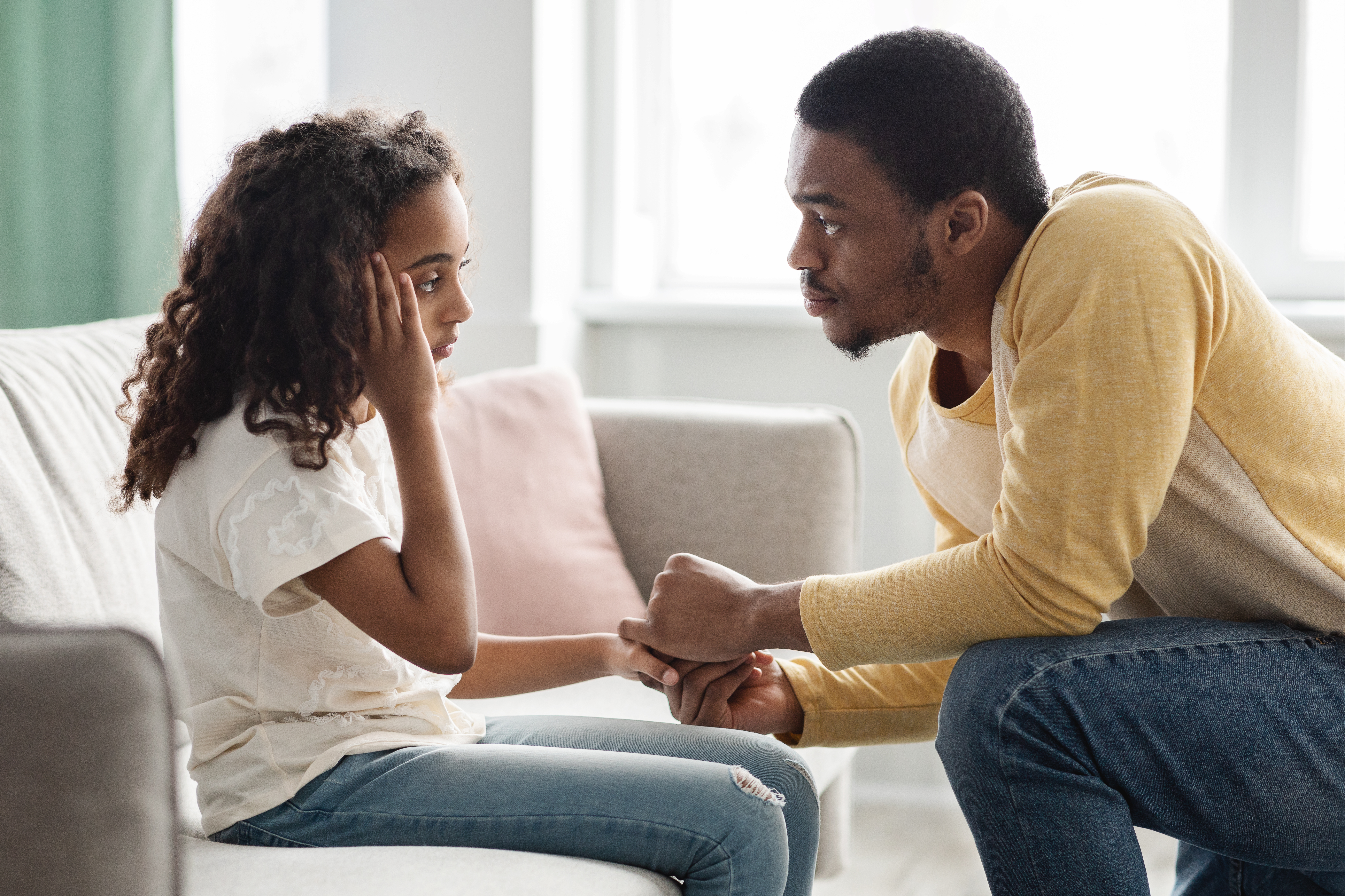 A father gently holds his child's hands, speaking in a calm, reassuring manner.