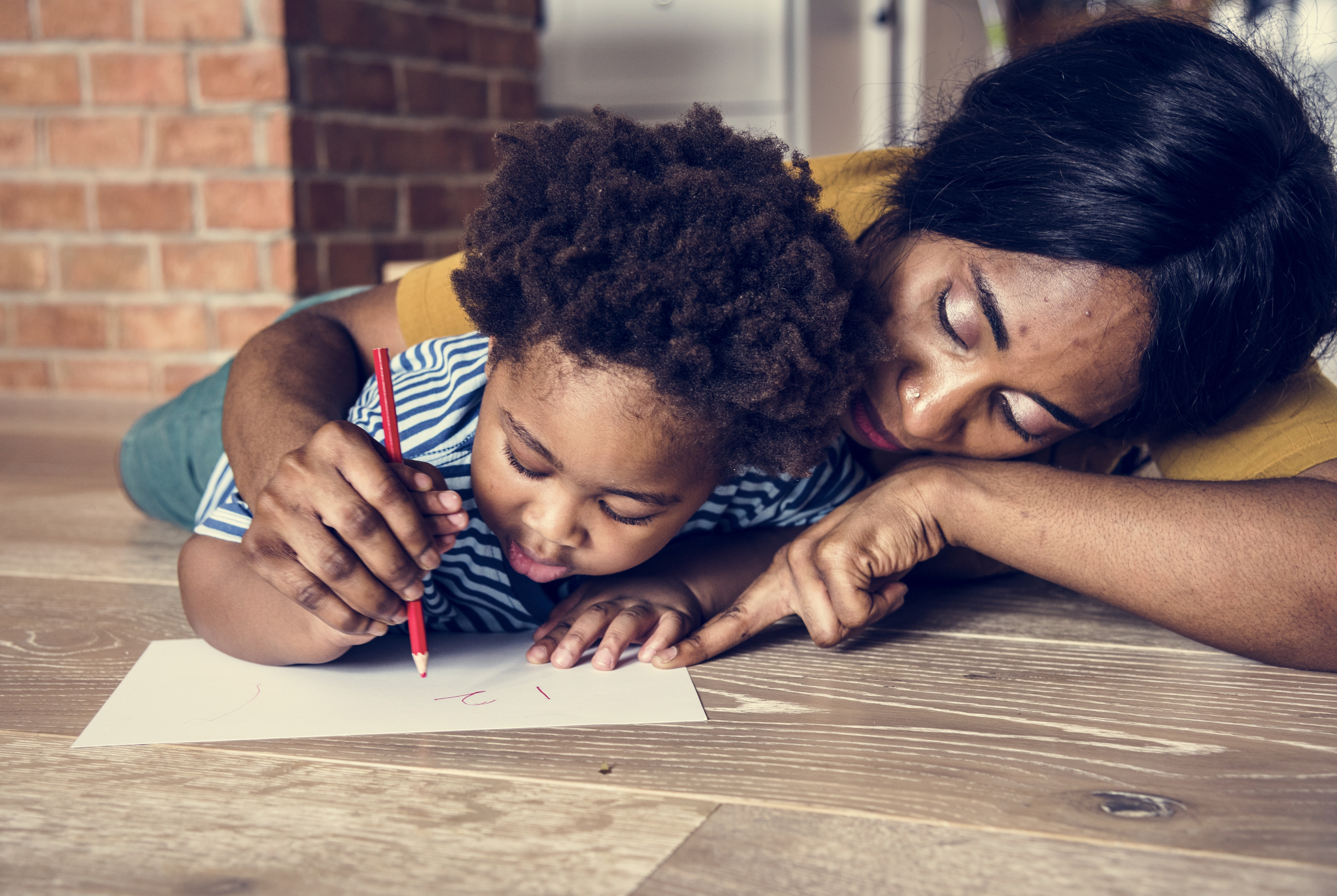 The mother patiently teaches her child the correct way to hold a crayon as a means of supporting their physical and social development. The mother patiently teaches her child the correct way to hold a crayon as a means of supporting their physical and social development.
