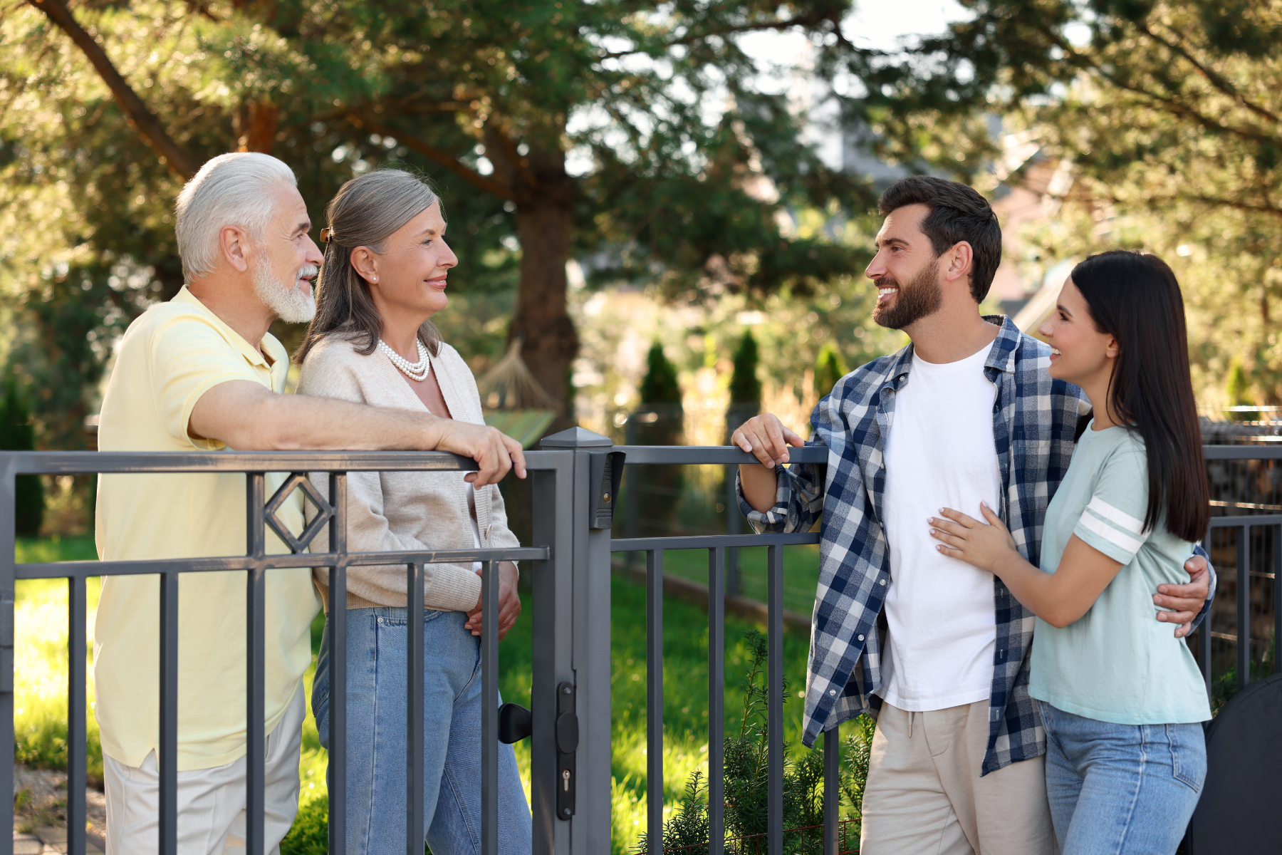 Two couples—one older and one younger—smiling and talking over a front yard fence in a suburban Northern Virginia neighborhood, symbolizing friendly community living and multi-generational connection. Two couples—one older and one younger—smiling and talking over a front yard fence in a suburban Northern Virginia neighborhood, symbolizing friendly community living and multi-generational connection.
