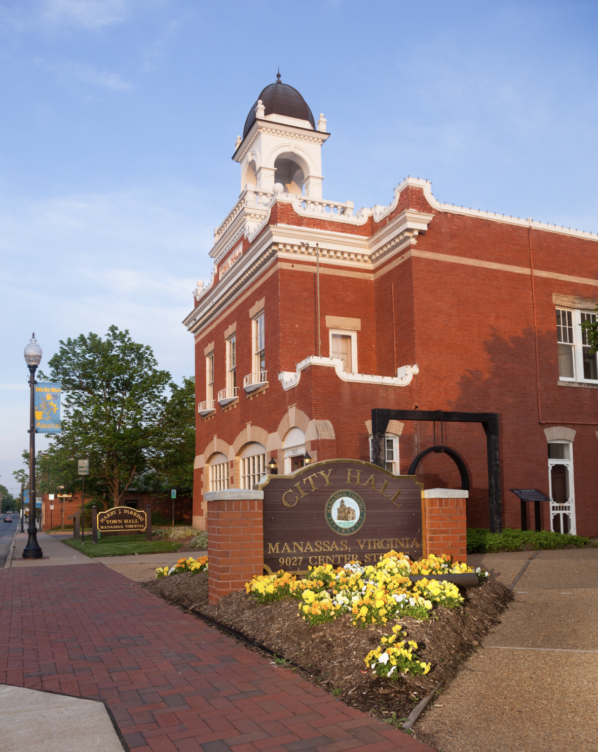 Historic red-brick Manassas City Hall in Virginia, featuring a white clock tower and surrounded by blooming yellow flowers and a welcoming sidewalk. Historic red-brick Manassas City Hall in Virginia, featuring a white clock tower and surrounded by blooming yellow flowers and a welcoming sidewalk.