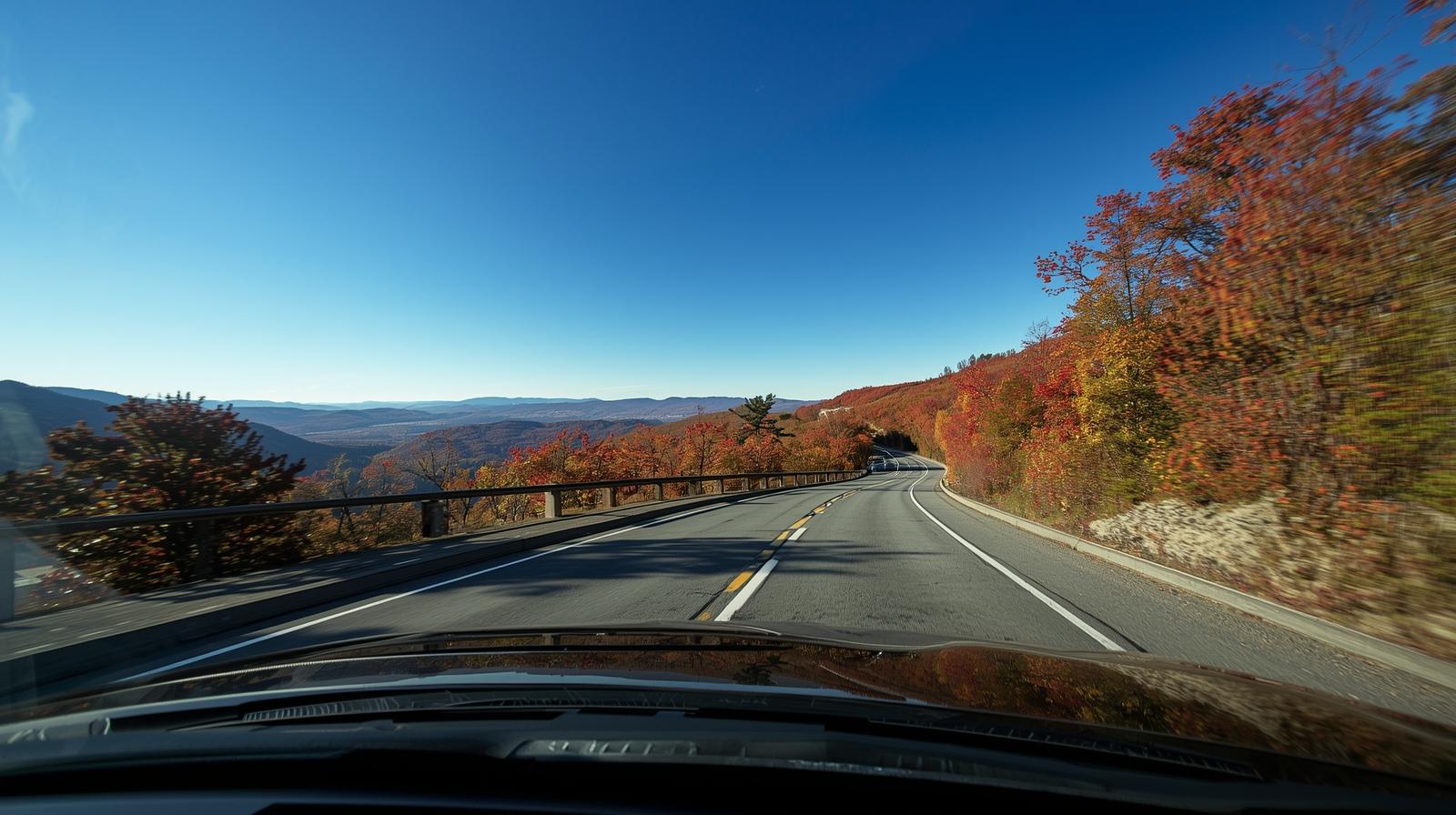 Car driving along Skyline Drive in Shenandoah National Park with early autumn foliage and mountain views under a blue sky.