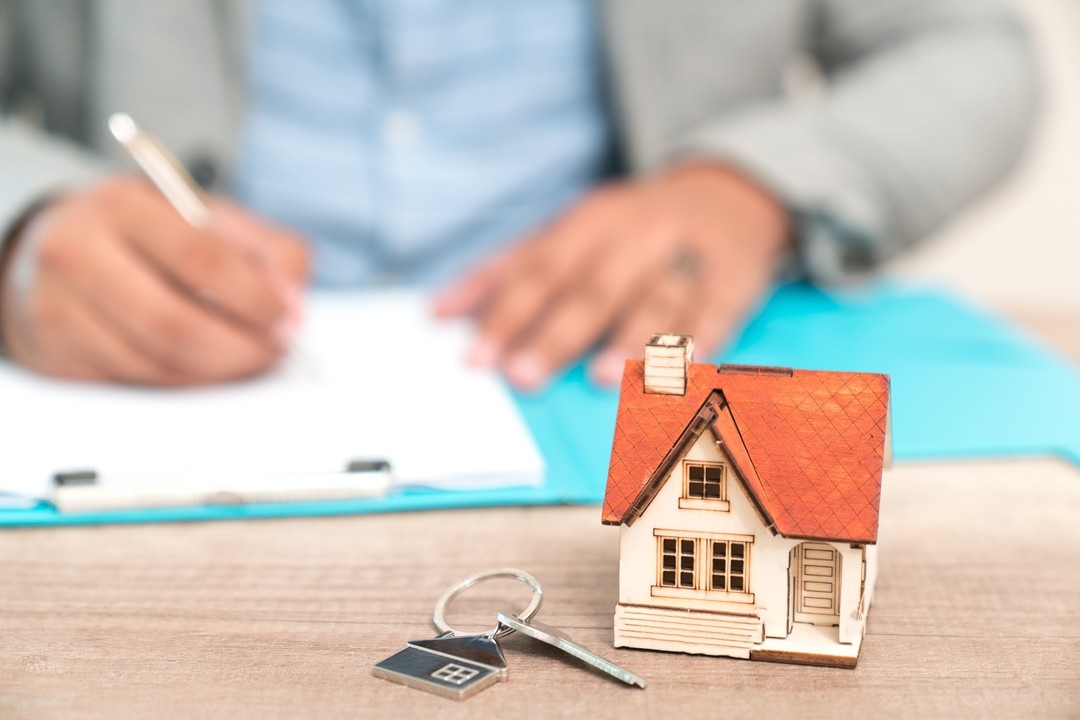  A real estate agent and client exchanging a house model with a pen, showcasing the benefits of REI CRM systems from AMPLIFIREI.