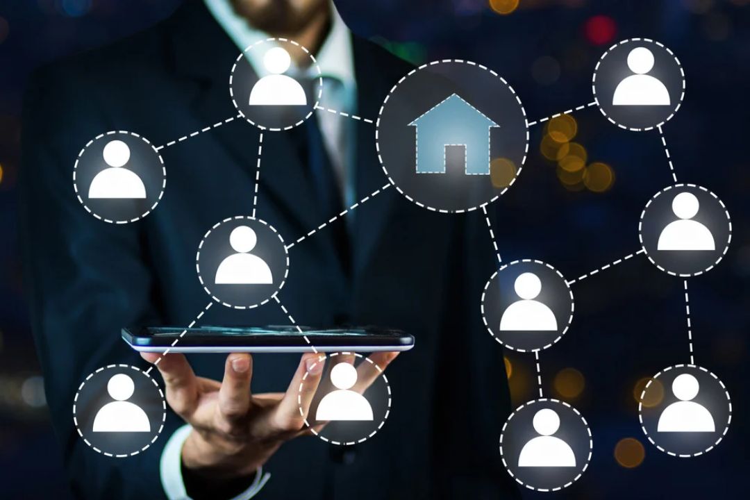 A man in a suit holds a tablet displaying a network of people connected to a house icon, representing AMPLIFIREI's tools for converting seller leads faster through connections. A man in a suit holds a tablet displaying a network of people connected to a house icon, representing AMPLIFIREI's tools for converting seller leads faster through connections.