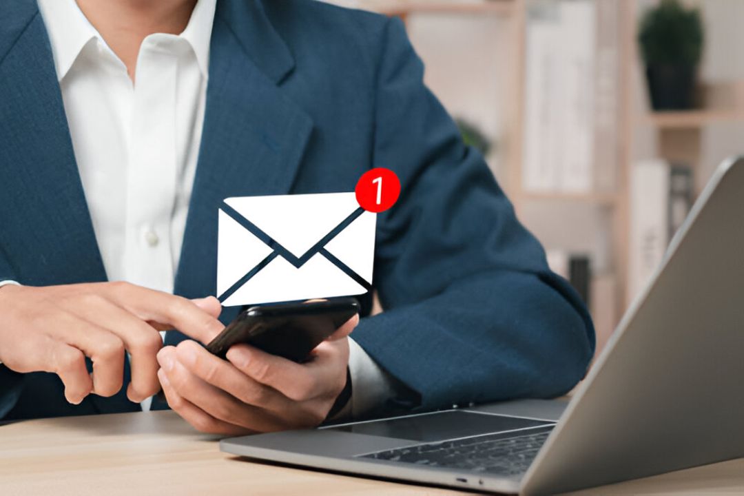 A businessman checks his phone with an email icon notification, illustrating AMPLIFIREI's strategy for integrating SMS and email in REI campaigns. A businessman checks his phone with an email icon notification, illustrating AMPLIFIREI's strategy for integrating SMS and email in REI campaigns.