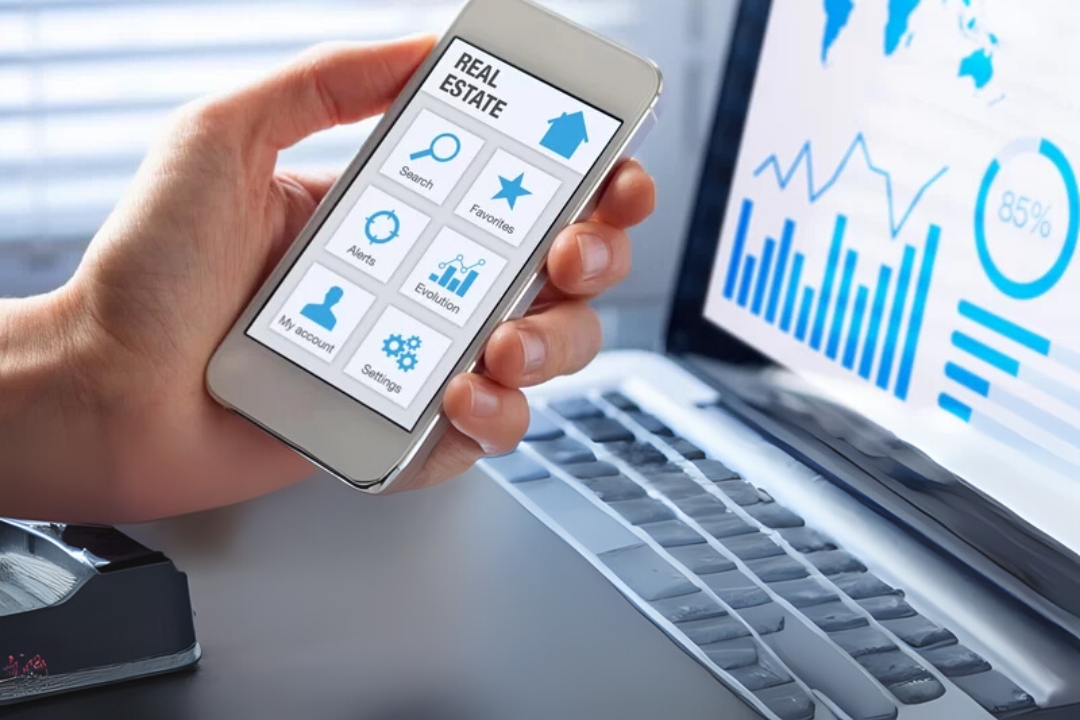 A person's hand holds a smartphone displaying a "REAL ESTATE" app next to a laptop with charts, illustrating AI-driven REI marketing platforms. A person's hand holds a smartphone displaying a "REAL ESTATE" app next to a laptop with charts, illustrating AI-driven REI marketing platforms.
