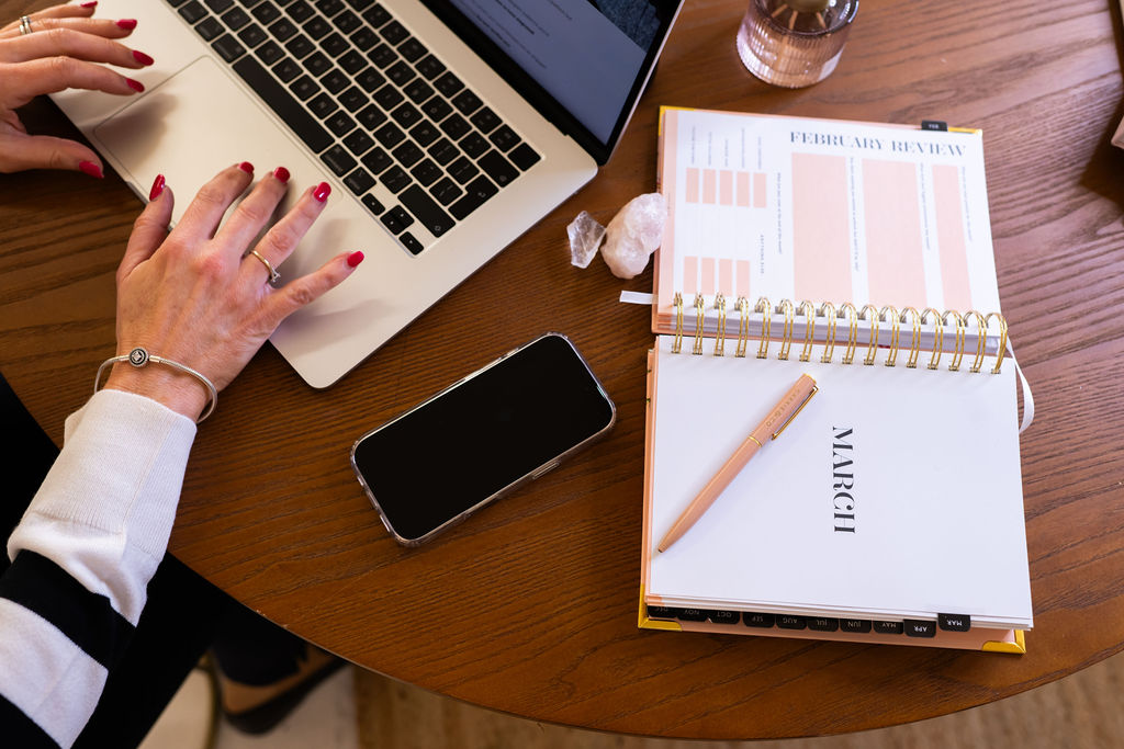 female working at a laptop with a planner open on the desk next to her