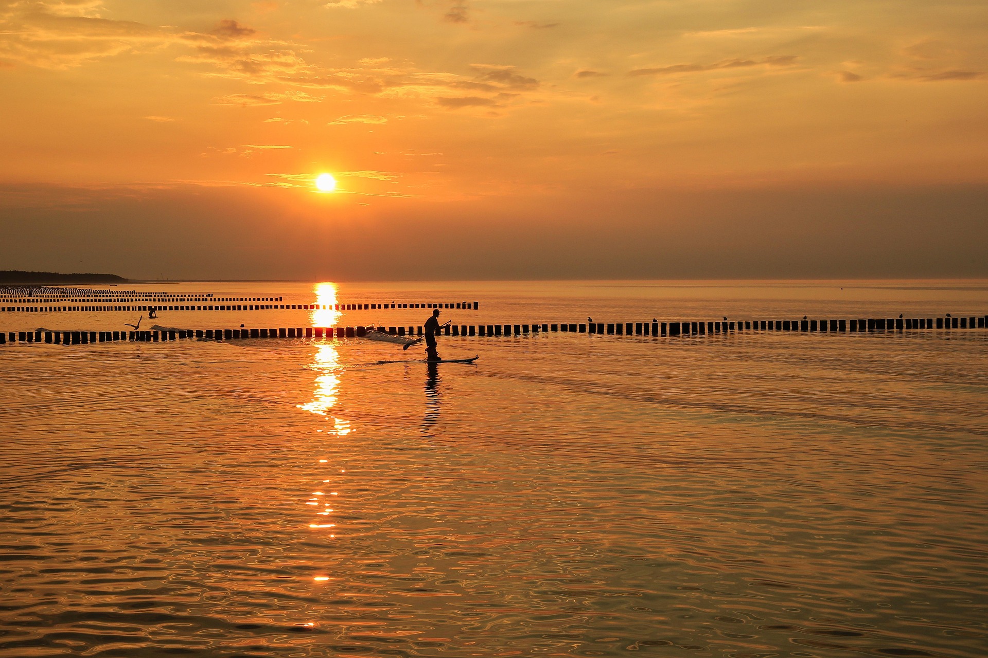 A person paddleboarding on calm water during a golden sunset, with the sun casting a warm reflection across the sea and a peaceful atmosphere all around. A person paddleboarding on calm water during a golden sunset, with the sun casting a warm reflection across the sea and a peaceful atmosphere all around.