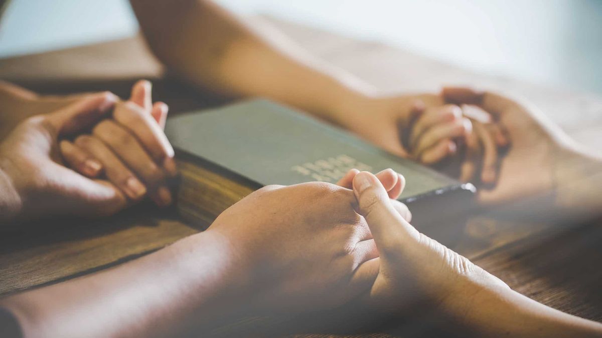 Christian family holding hands in prayer around an open Bible at home, symbolizing faith beginning in the home, family devotion, and building a Christ-centered household.