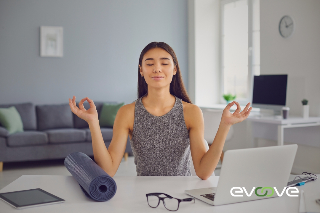 "A professional woman takes a mindful break at her home office, meditating with a yoga mat beside her, showcasing work-life balance. The Evoove logo emphasizes the importance of staffing solutions that support well-being and productivity.