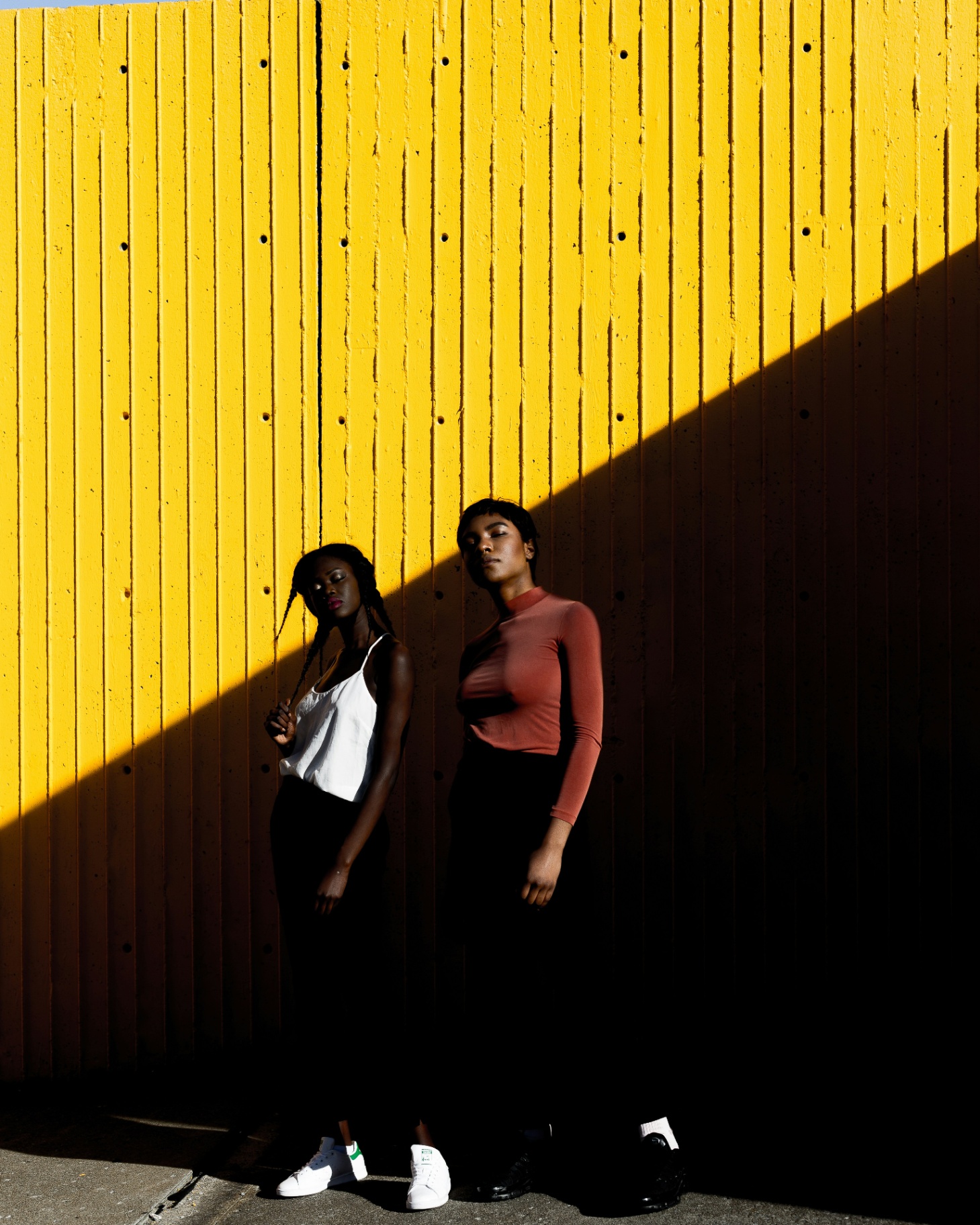 Two women against yellow wall with dramatic shadows