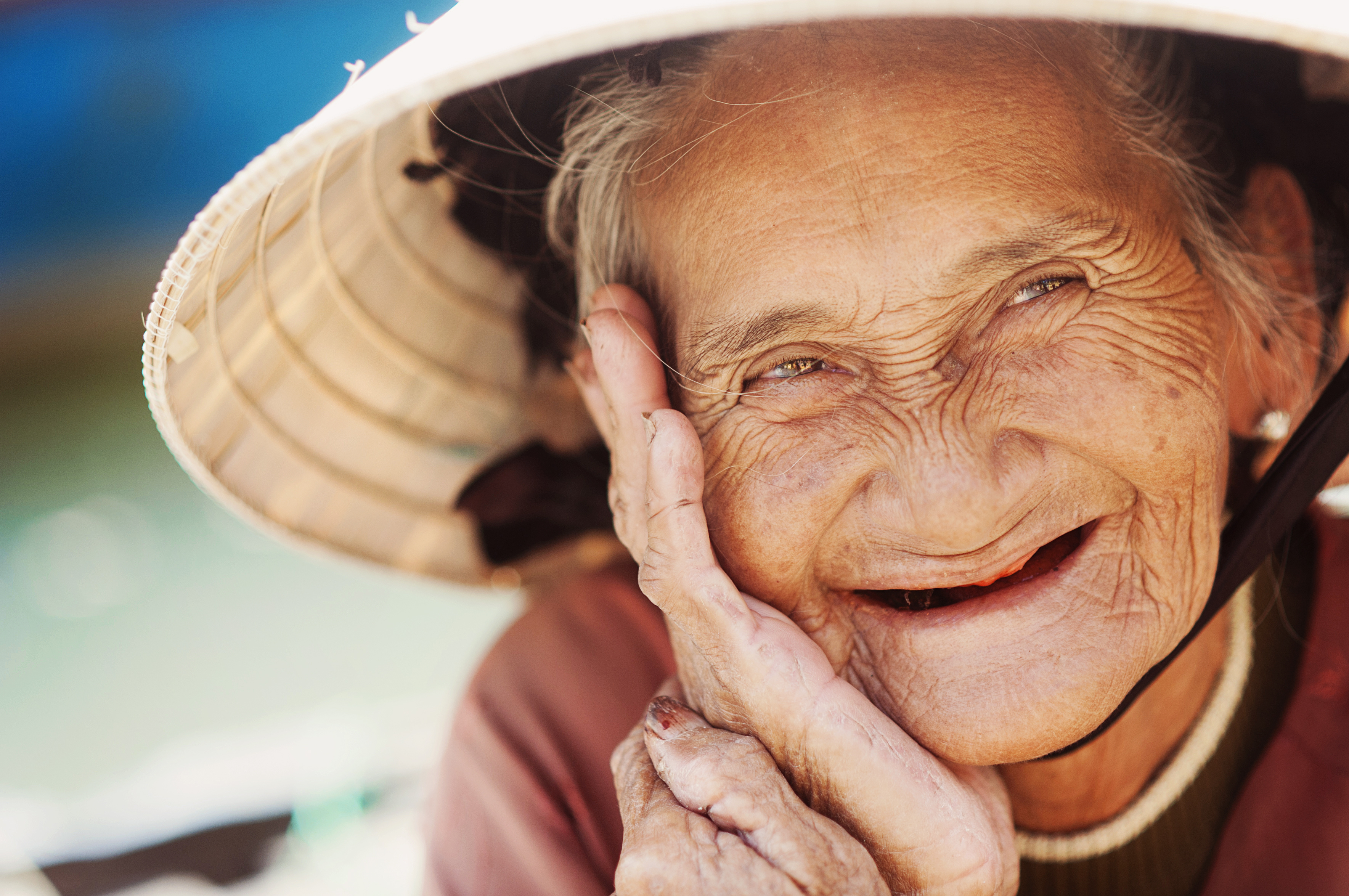 An elderly Asian woman with a deeply lined face looks directly into the lens with a delightful smile. By @Halfpoint via Adobe Stock