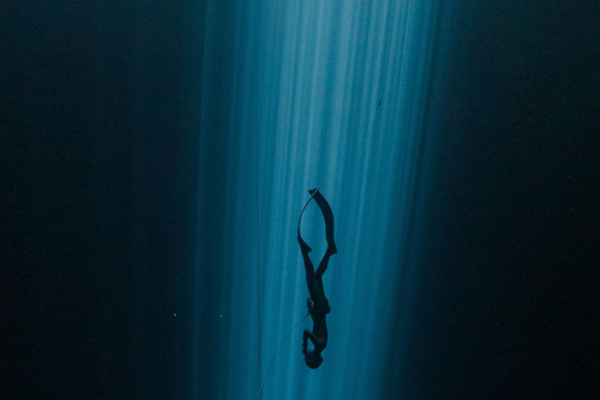 deep sea diver in the light of the sun shining through dark water