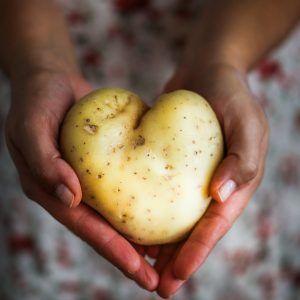 hands holding a potato shaped like a heart