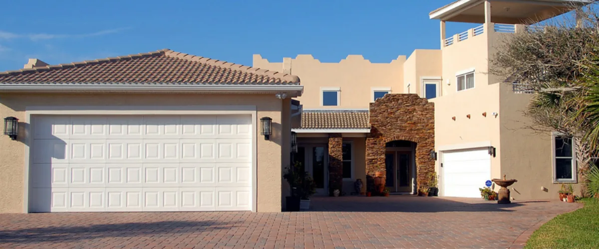 Stucco home with large white garage door and paved driveway in a residential neighborhood.