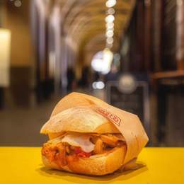 Close-up of an Italian panini with the historic Padua marketplace blurred in the background
