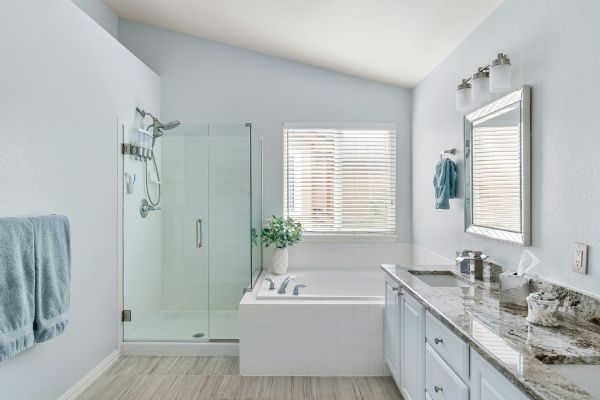 Bright modern bathroom with glass shower, soaking tub, granite countertop, and white cabinets.