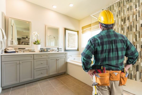 Contractor in hard hat inspecting a modern bathroom with double vanity, bathtub, and tiled shower wall.