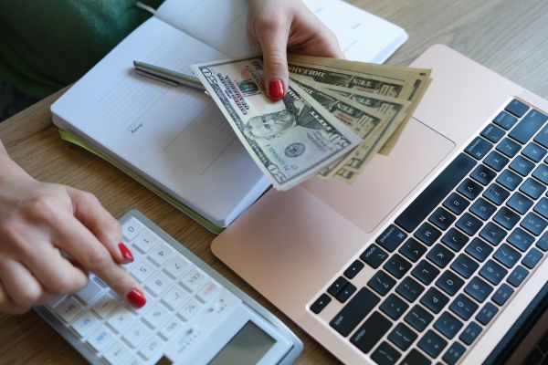 Person budgeting with cash, calculator, and laptop