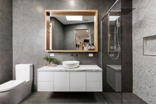 Modern bathroom with dark gray tiles, floating vanity, large wooden-frame mirror, and glass shower enclosure.