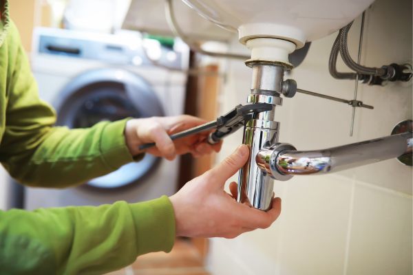 Plumber fixing a sink pipe with a wrench in a residential bathroom or laundry room