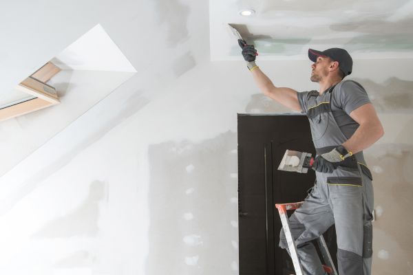 Construction worker applying drywall plaster to a ceiling during home renovation