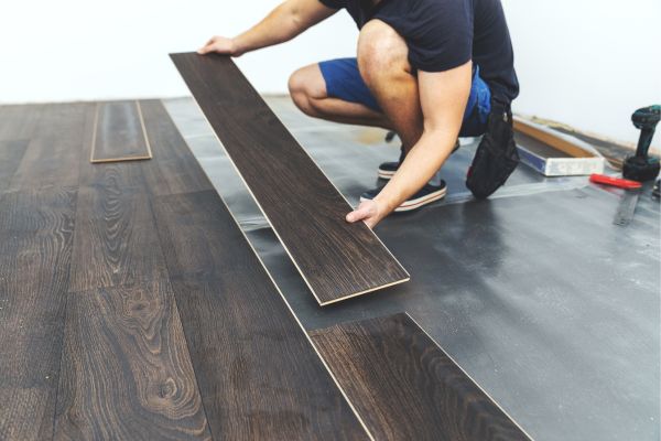 Worker installing dark wood laminate flooring in a modern home